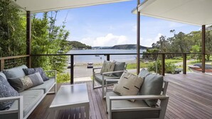 A covered outdoor seating area with a view of a lake and hills. - Luxury Villas Araluen Waterfront Getaway (Walk to the beach) (Central Coast)