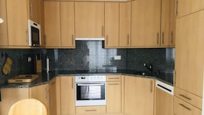 A compact kitchen with wooden cabinets, a microwave, oven, and a sink. - Edelweiss A by Interhome (Leukerbad)
