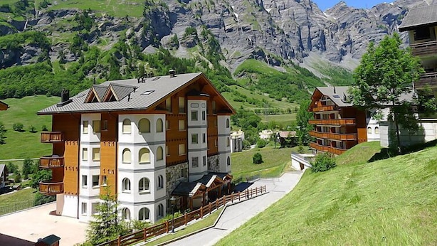A chalet-style building with a sloped roof, multiple balconies, and a view of a mountainous landscape. - Edelweiss A by Interhome (Leukerbad)