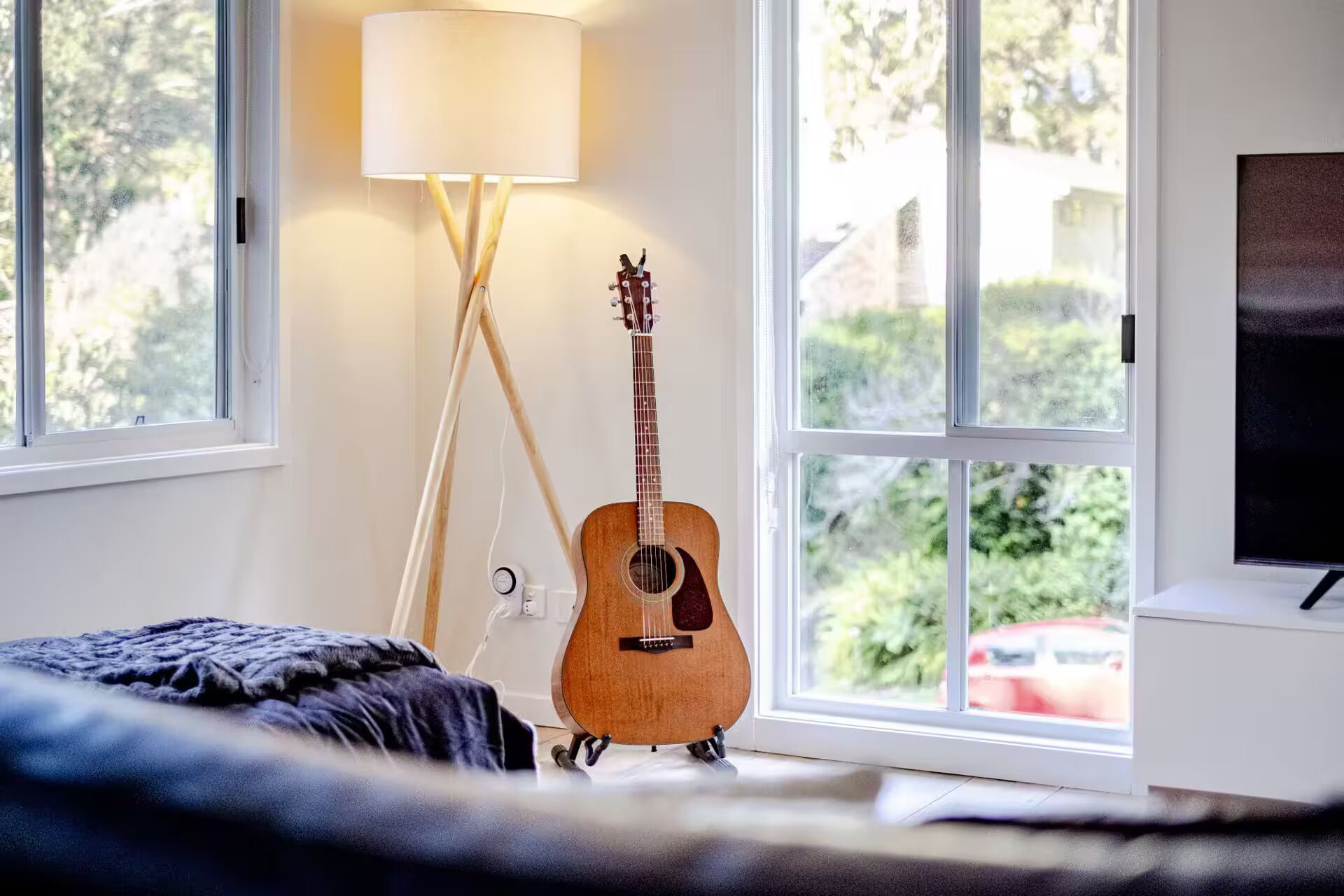 Une pièce avec un lit, une guitare, une lampe et un téléviseur.
