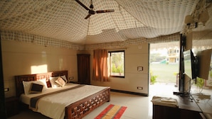 Quarto com cama, ventilador de teto, janela e televisão sobre um móvel de madeira.