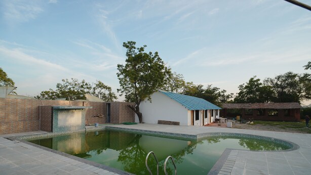 Uma piscina com borda curva, um pequeno edifício com telhado azul e uma parede de tijolos.