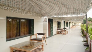Uma área de estar coberta ao ar livre, com teto estampado, cadeiras de madeira e piso ladrilhado.