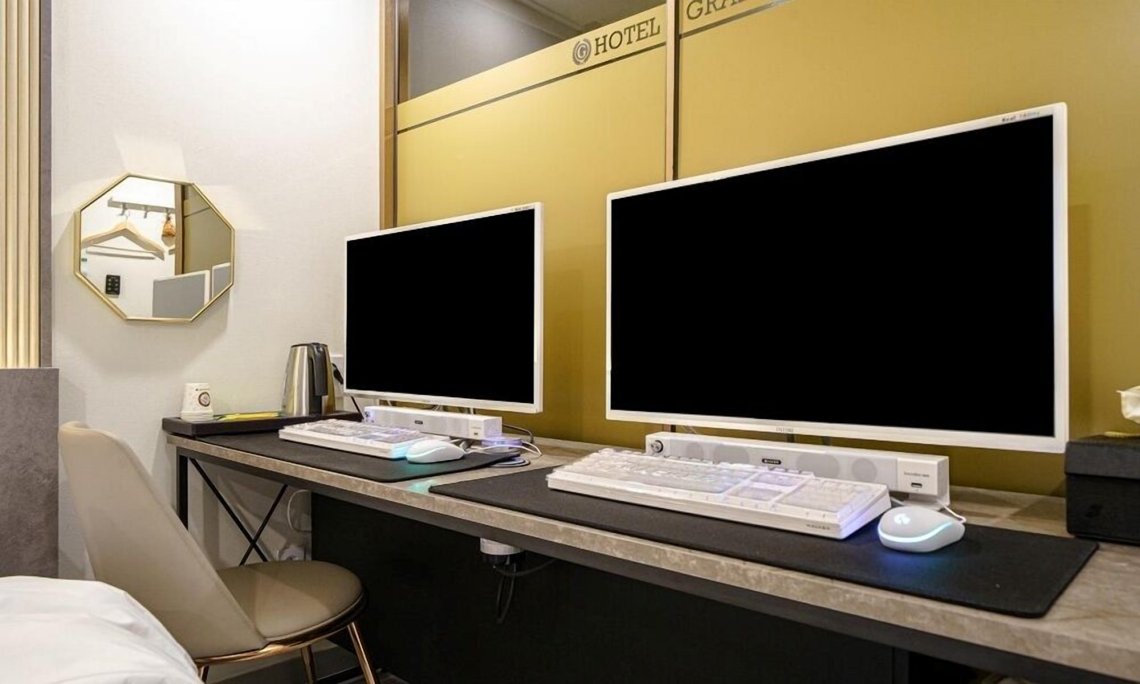 A hotel reception desk with two large monitors, a keyboard, a mouse, and a coffee machine.