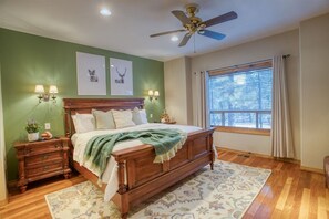 Quarto com cama de madeira, duas luminárias na parede, ventoinha no teto, janela com cortinas e parede verde.