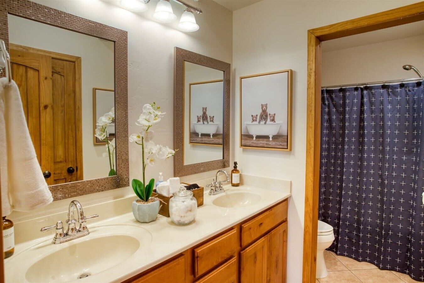 Une salle de bain avec deux lavabos, un miroir, un rideau de douche et des toilettes.