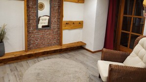 A room with a brick wall, wooden beams, a mirror, a cushioned chair, and a large window with curtains. - Schöne Große Ferienwohnung für 1-4 Gäste, zum Entspannen Bestens Geeignet (Frielendorf)