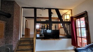 A staircase leading to a loft area with exposed beams, a television mounted on a wooden platform, and a red curtain on a window. - Schöne Große Ferienwohnung für 1-4 Gäste, zum Entspannen Bestens Geeignet (Frielendorf)