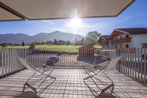 Une terrasse avec vue sur les montagnes, un espace clos avec des chaises et un bâtiment doté d’un balcon.
