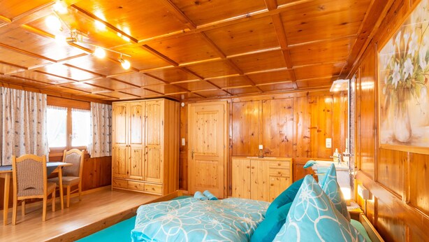 Ein Holzblockhaus-Innenraum mit Bett, Essbereich und Bad.