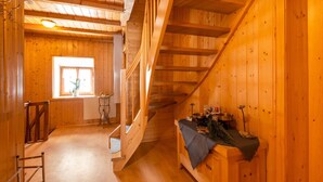 Ein Holzhütten-Innenraum mit Treppe, einem kleinen Tisch mit Gegenständen und einem Fenster mit Tageslicht.