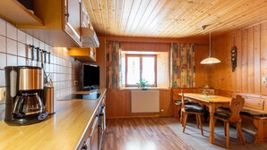 Ein Holzinterieur mit einer Küche und Essbereich, einschließlich eines Herdes, einer Kaffeemaschine und einem Esstisch mit Stühlen.
