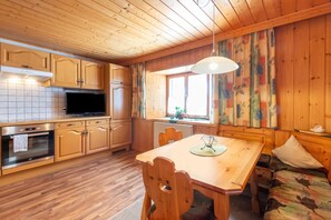Interior de uma cabana de madeira com cozinha, sala de jantar e uma janela com cortinas.