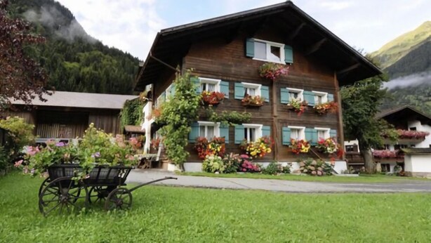 Eine Holzchalet mit zahlreichen Fenstern, umgeben von üppigem Grün und Blumen.