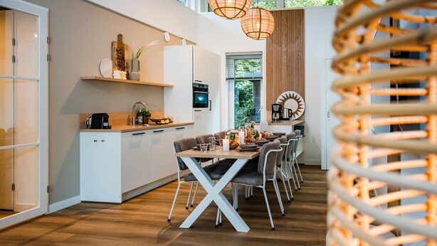 Een moderne keuken met witte kastjes, een houten aanrecht en een eethoek met een witte tafel en stoelen.