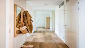 A hallway with wooden flooring, a coat rack with hanging items, and a pair of slippers on the floor.