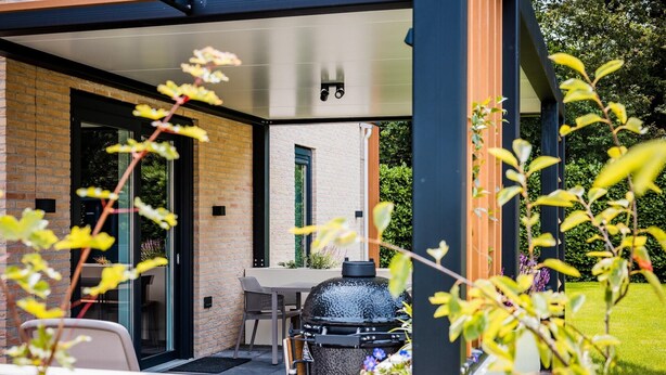 A patio area with a grill, a table, and chairs, surrounded by a brick wall and glass doors.