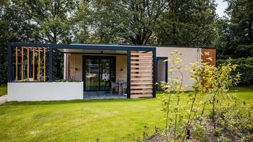 A modern house with a glass door entrance, a small patio with a table and chairs, and a garden area with various plants.