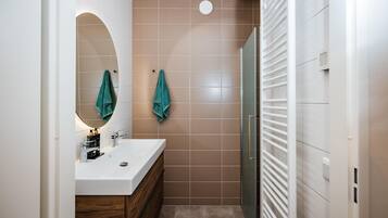 Une salle de bain moderne avec un lavabo blanc, un meuble-lavabo en bois, deux serviettes vertes et une cabine de douche en verre.
