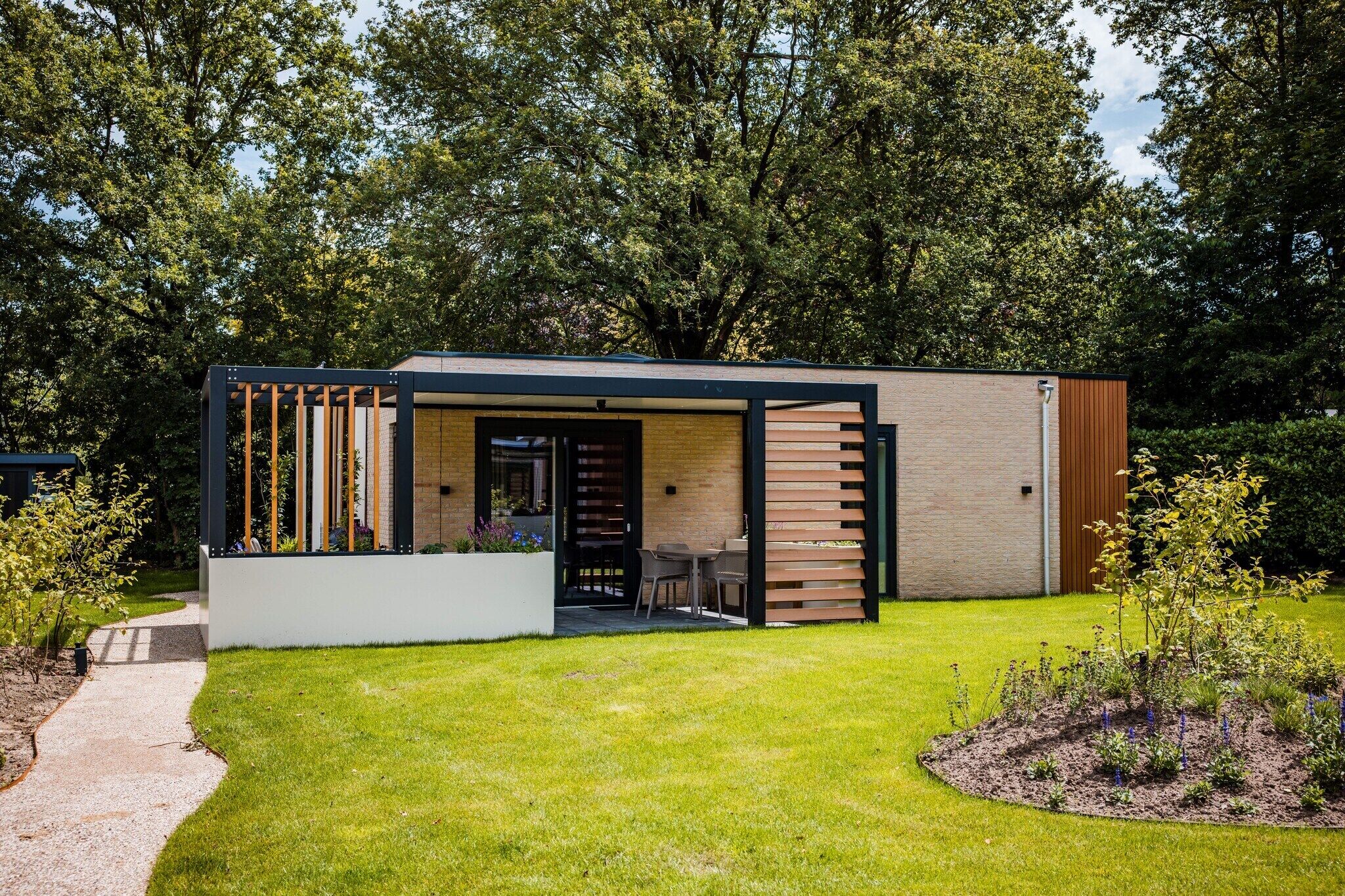 Een modern, gelijkvloers huis met een overdekt terras, een kleine tuin en een pad dat naar de ingang leidt.