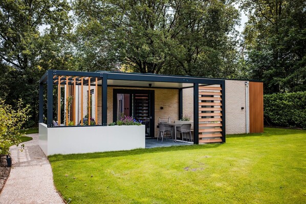 A modern outdoor structure with a patio, seating, and a door leading to an interior space.