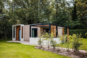 A modern house with a covered outdoor area, surrounded by a well-maintained garden and trees. - Chalet in Voorthuizen near Veluwe Nature (Voorthuizen)