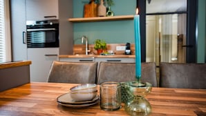 A modern kitchen with a teal-colored candle, a glass candle holder, and a set of plates on a wooden table. - Chalet in Voorthuizen near Veluwe Nature (Voorthuizen)