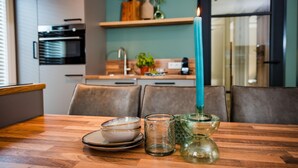 A dining table with plates, a candle, and glassware in a modern kitchen with a teal backsplash and wooden cabinets. - Calming Hideaway in Veluwe (Voorthuizen)