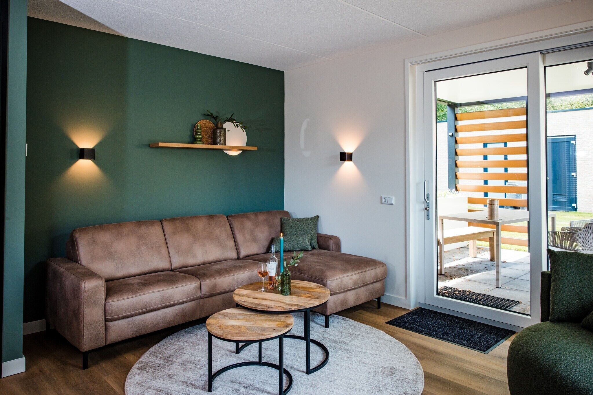 Una sala de estar moderna con un sofá de cuero marrón, dos mesitas de madera y una pared de acento verde.
