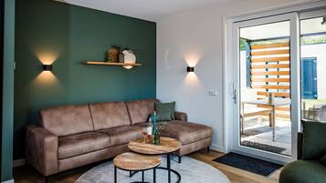 Una sala de estar moderna con un sofá de cuero marrón, dos mesitas de madera y una pared de acento verde.