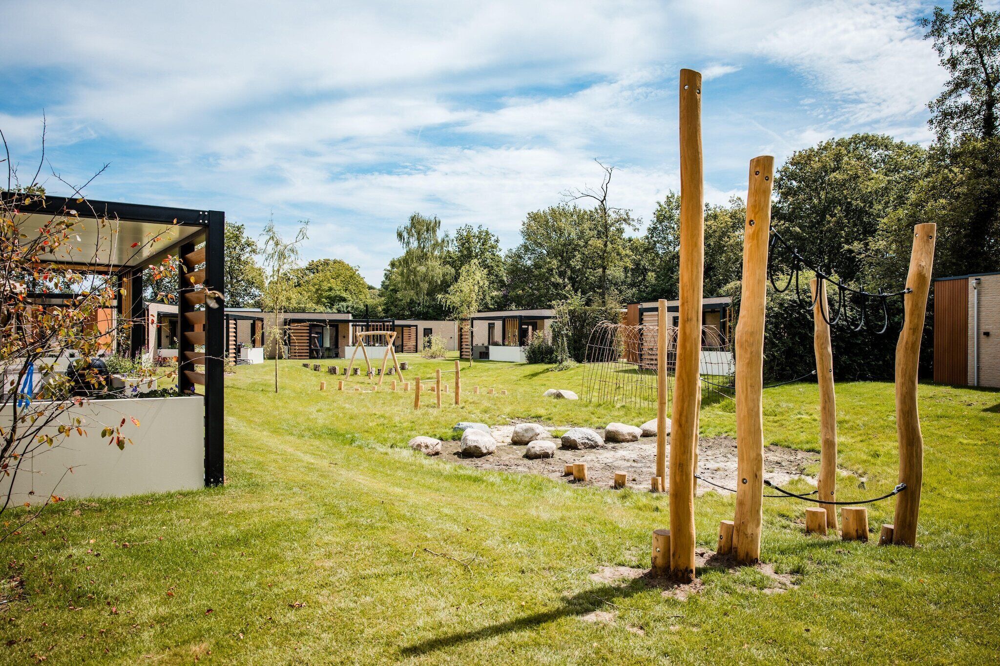 A modern outdoor area with a grassy lawn, wooden posts, and a building with large windows.