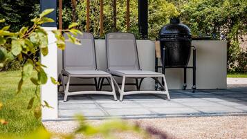 A patio with two grey chairs and a black barbecue grill.