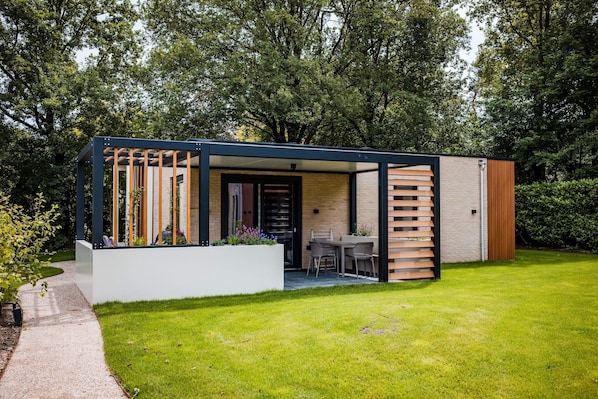 A modern outdoor structure with a patio, seating, and a door leading to an interior space.