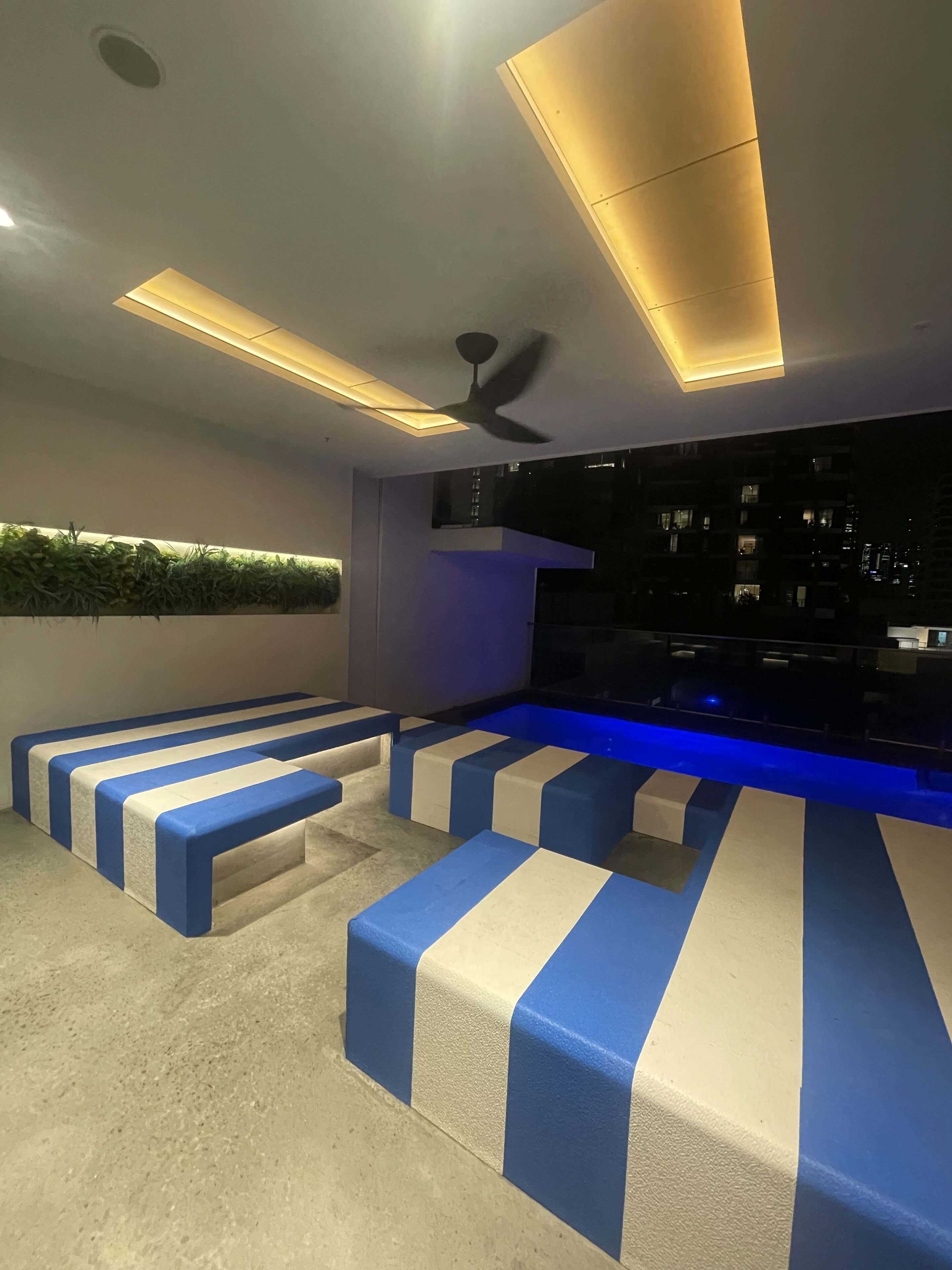 A modern living room with a pool table, blue and white striped seating, recessed lighting, and a ceiling fan.