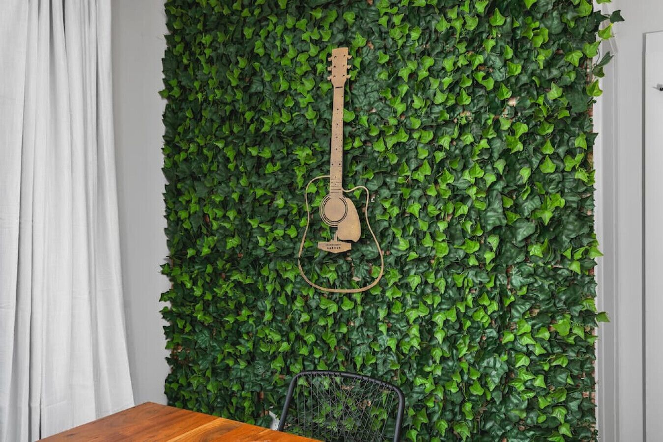 A guitar hanging on a wall covered with green leaves.