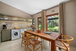 A modern kitchen with a dining area, a washing machine, and a view of a garden.