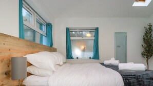 Une chambre d’hôtel avec une tête de lit en bois, un lit avec une literie blanche, une table de chevet avec une lampe, une fenêtre avec des rideaux et une plante.