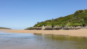 Une plage avec un rivage sablonneux et une colline herbeuse, sur laquelle se trouve un escalier menant à une construction.