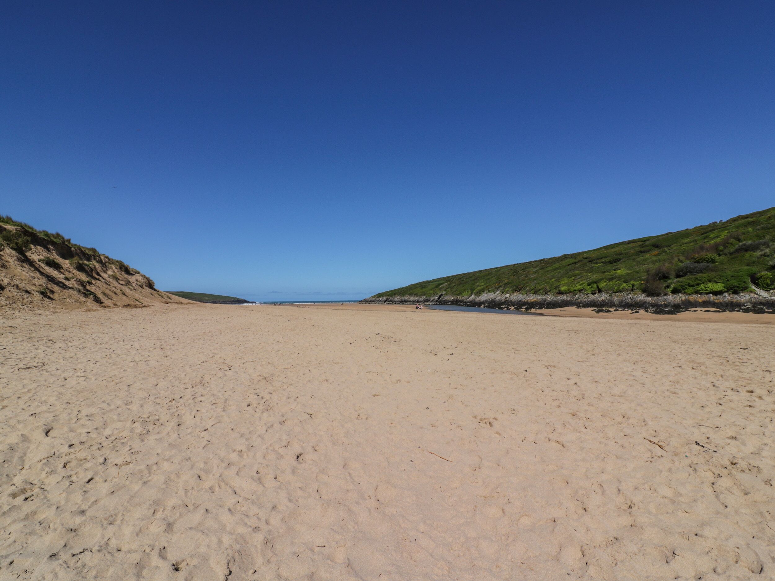 A wide sandy beach with gentle slopes on both sides, leading to a calm sea.