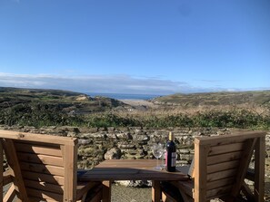 A wooden table with two chairs facing a scenic view of hills and a beach.