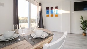 Un espace repas avec une table en bois, des chaises blanches et une vue sur l’extérieur.