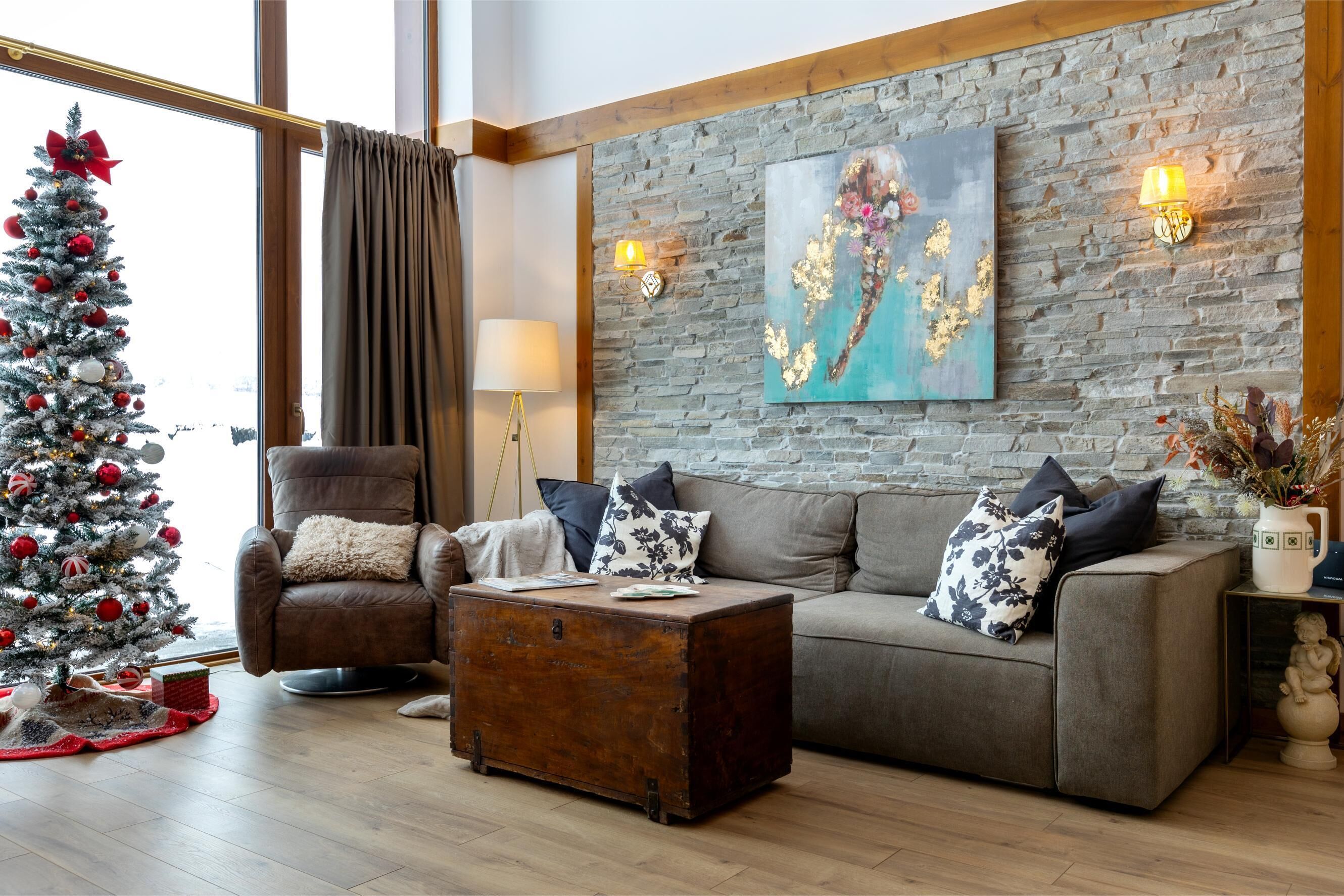 Un salon chaleureux avec un sapin de Noël, un fauteuil en cuir, un canapé et un tableau accroché au mur.