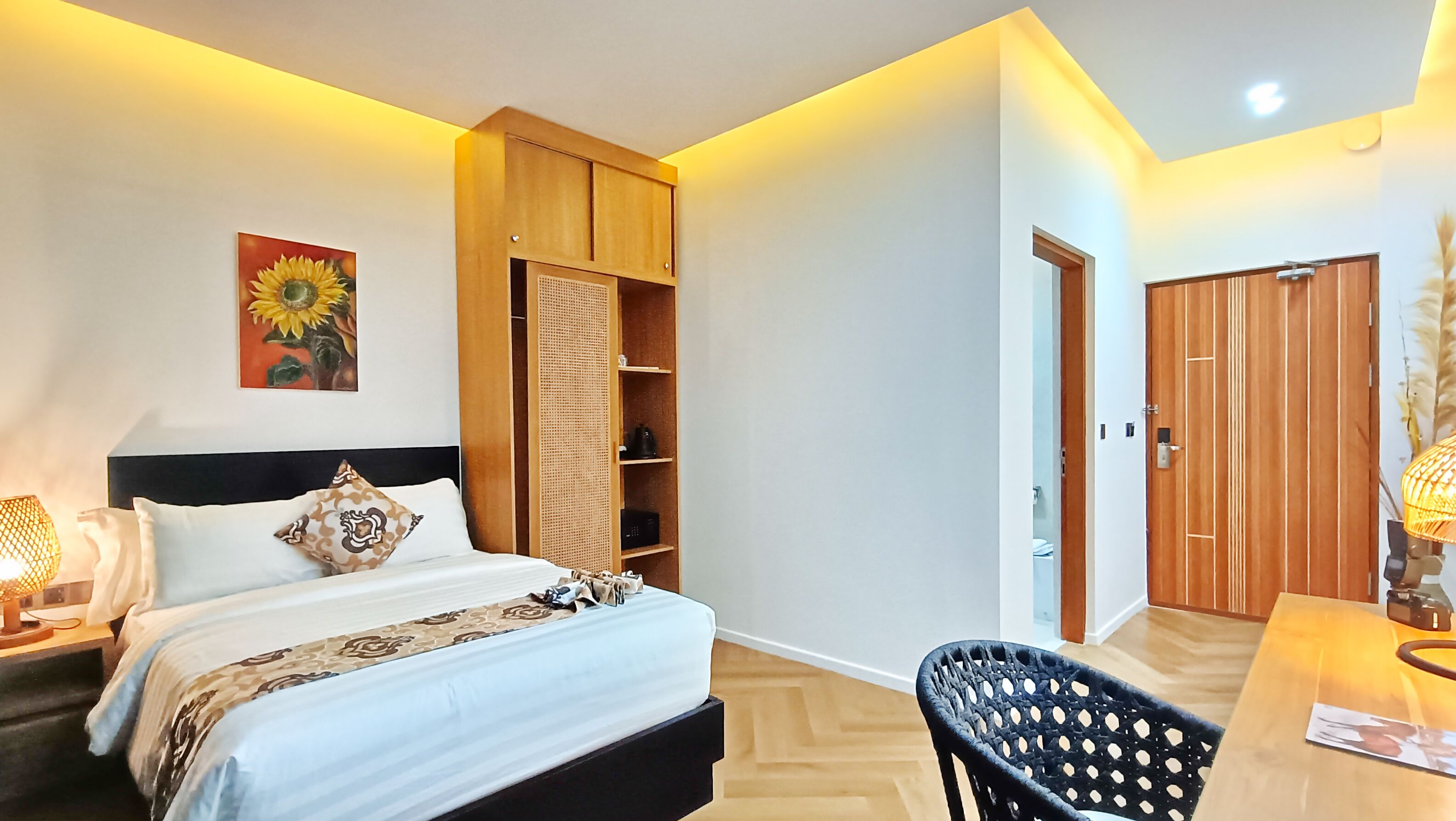 Ein Schlafzimmer mit Bett, Nachttisch, Lampe, einem Holzschrank und einem Schreibtisch mit Stuhl.