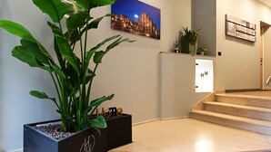 A modern interior with a staircase, a potted plant, a framed cityscape picture, and a small shelf with decorative items. - Holiday Homes Aparthotel Milano (Milan)