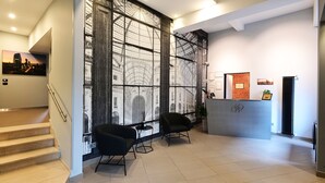 A modern reception area with a staircase, two black armchairs, a reception desk, and a large window with a cityscape view. - Holiday Homes Aparthotel Milano (Milan)