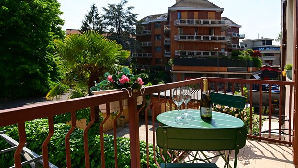 A balcony with a table and chairs, a bottle of wine, and a view of a multi-story building with balconies. - Holiday Homes Aparthotel Milano (Milan)