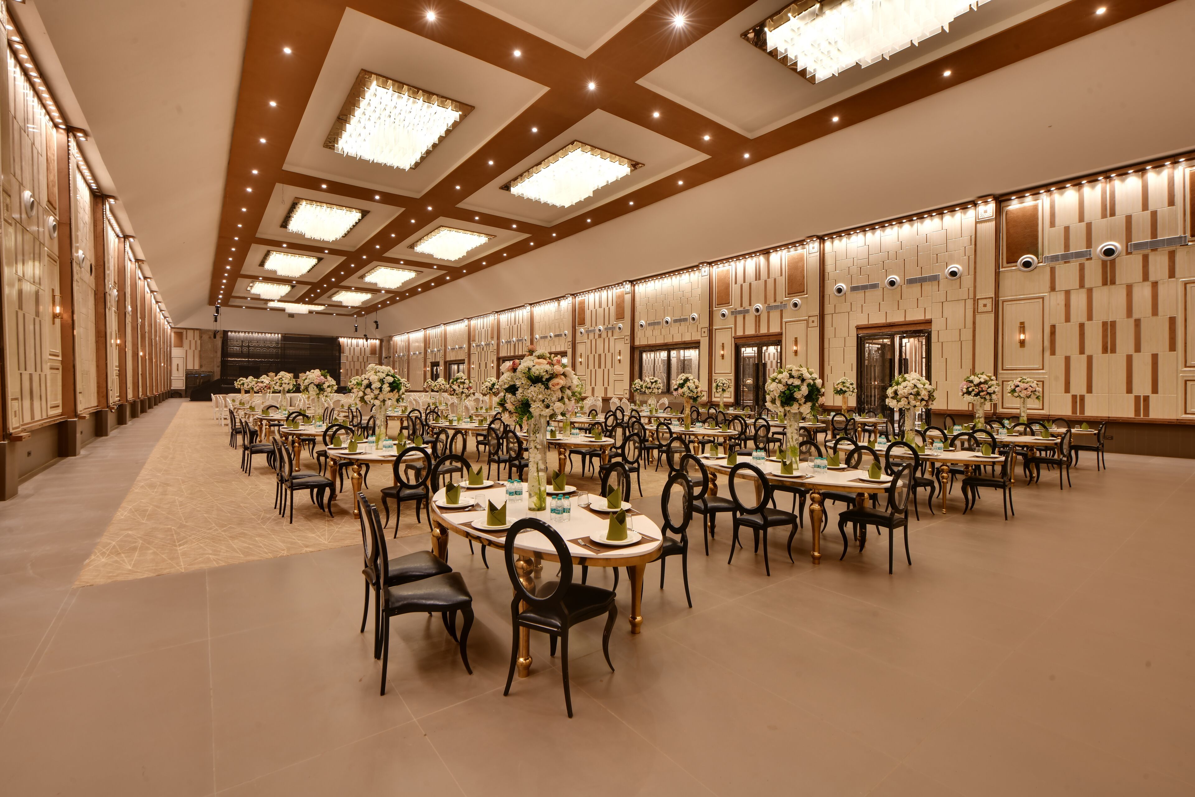 A spacious banquet hall with multiple round tables, each set with chairs and floral centerpieces.