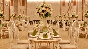 A banquet hall with ornate white chairs, round tables, and floral centerpieces.
