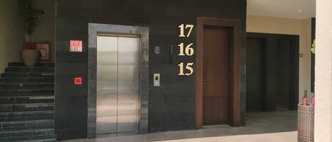 A building entrance with a staircase, an elevator, and a door marked with numbers 17, 16, and 15.