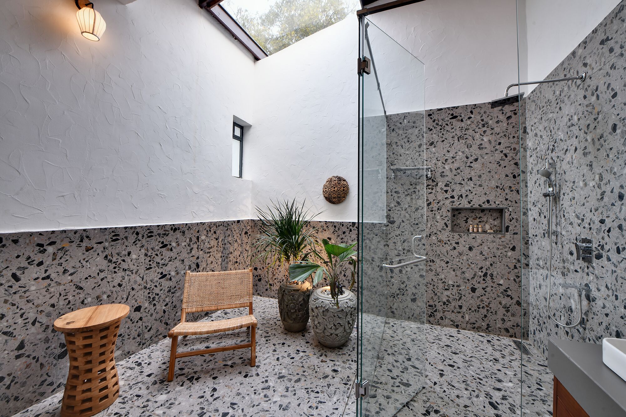 A modern bathroom with a glass shower enclosure, a wooden chair, and decorative plants.